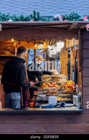Venditori ambulanti che preparano cibo di strada tradizionale in un mercatino di Natale a Breslavia, Polonia. Bancarelle in legno con carne alla griglia, salsicce e pane, captur Foto Stock