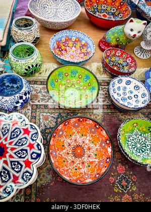 Mostra colorata di ciotole in ceramica finemente dipinte, lampade a mosaico e una statuetta decorativa di gatto su un tappeto di mercato a motivi geometrici Foto Stock