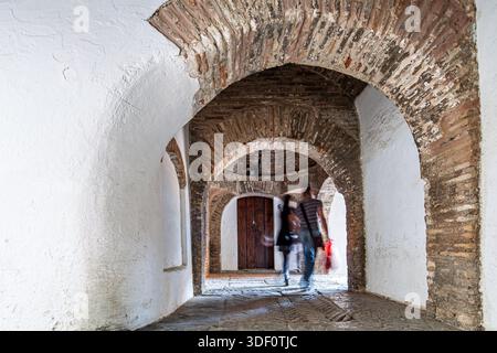 La coppia cammina attraverso gli archi di Callejon de la Juderia nel Barrio de Santa Cruz di Siviglia, in Spagna. Una scena di viaggio europea storica e senza tempo. Foto Stock