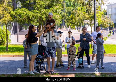 Diversi gruppi di persone godono di una soleggiata giornata estiva al parco dopo la parata della vittoria a Bishkek, Kirghizistan - 8 maggio 2025 Foto Stock