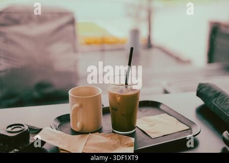 Latte ghiacciato e tazza vuota su un vassoio vicino alla finestra Foto Stock