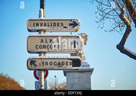 Primo piano di cartelli stradali ricoperti di neve a Parigi, Francia, che mostrano le indicazioni per Invalides, Alma, Concorde e Trocadero catturati in una brillante giornata invernale Foto Stock