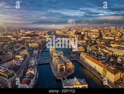 Vista dall'alba del paesaggio urbano di Ginevra, Svizzera, durante una mattina nebbiosa d'inverno con sole e nuvole Foto Stock