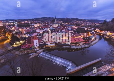 Vista del fiume Moldava che si snoda intorno agli edifici illuminati con tetti rossi sotto un cielo crepuscolo, riflettendo il fascino della città al crepuscolo, Cesky Krumlov, Foto Stock