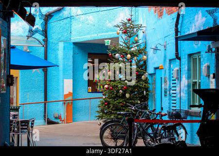 Oxford, Regno Unito - 22 dicembre 2025: Un cortile con pareti blu brillante. Un albero di Natale decorato al centro della composizione. Foto Stock