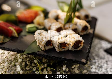 Una selezione di sushi roll, tonno, salmone e guarnigioni è organizzata su un tabellone di ardesia nero. L'illuminazione soffusa mette in risalto le texture e i colori freschi di Foto Stock