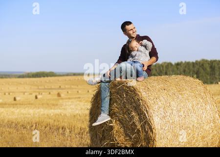 Padre Felice e 2 anno vecchia ragazza seduta su balle di fieno nel campo di raccolto Foto Stock