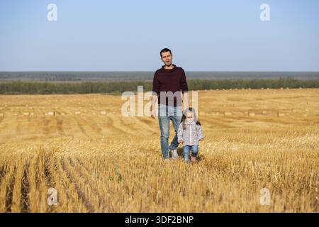 Felice padre e bambina di 2 anni che camminano nel campo raccolto Foto Stock