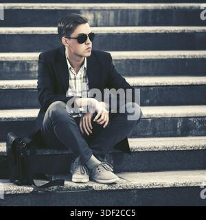 Moda giovane uomo in occhiali da sole seduti sui gradini Foto Stock