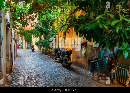 Una stretta strada acciottolata ombreggiata dal verde nel quartiere Monti di Roma, Italia. Foto Stock
