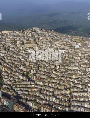 Veduta aerea degli edifici densamente affollati che scendono lungo la collina in un arazzo testurizzato di tetti in terracotta e pietra baciata dal sole, Gangi, Sicilia Foto Stock