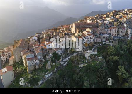 Vista aerea di un villaggio rustico aggrappato alla ripida collina, bagnato dal soffice bagliore del sole mattutino, Pollina, Sicilia, Italia. Foto Stock