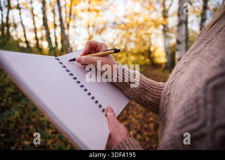 Primo piano di una donna che scrive a mano in diario all'aperto. La scrittura creativa e la consapevolezza pratica in natura Foto Stock