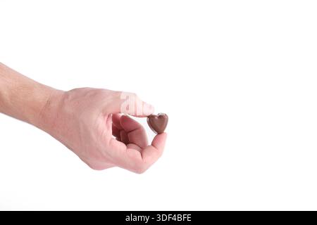 La mano dell'uomo che tiene le caramelle al cioccolato in forma il cuore è su sfondo bianco Foto Stock