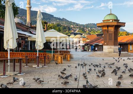 Sarajevo, Bosnia ed Erzegovina - 15 agosto 2022: I piccioni si riuniscono intorno alla fontana di legno di Sebilj in piazza Bascarsija nella città vecchia di Sarajevo con i suoi caffè Foto Stock