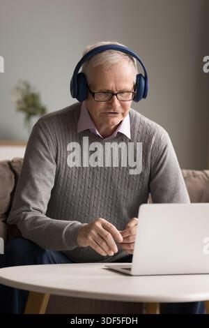 Uomini maturi che indossano auricolari che parlano tramite teleconferenza utilizzando il notebook Foto Stock