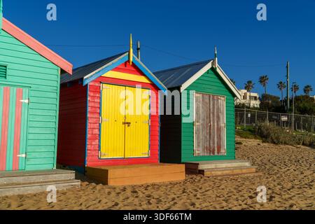 Tre case da spiaggia dai colori vivaci, con design e porte unici, fiancheggiano una spiaggia sabbiosa sotto un cielo limpido e soleggiato. Foto Stock
