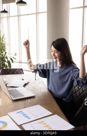 Giovane donna asiatica gioiosa che celebra la crescita delle vendite online Foto Stock
