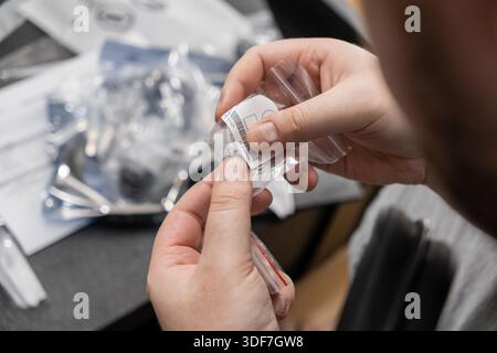 Primo piano mostra le mani professionali che tengono in mano un sacchetto di plastica trasparente con componenti di piccole dimensioni e un codice a barre, illustrando il montaggio preciso, l'ispezione di qualità, Foto Stock