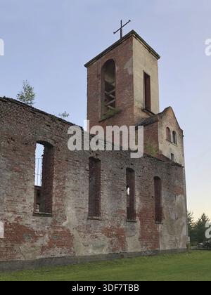 Il campanile con una croce sorge sopra le rovine di una vecchia chiesa, pareti in mattoni non intonacati con aperture vuote per le finestre Foto Stock