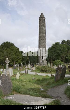 Glendalough, co. Wicklow, Irlanda - Agosto 10 2019 :Torre rotonda in pietra e alcune rovine di un insediamento monastico originariamente costruito nel VI secolo in G. Foto Stock