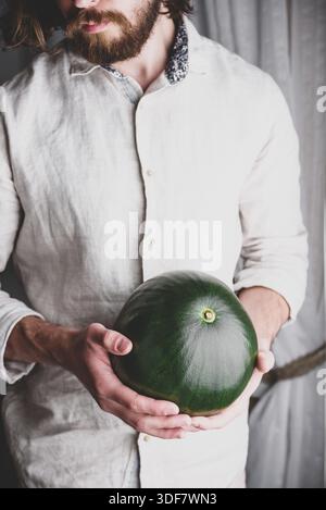 L'uomo portato in camicia di lino tiene nelle sue mani tutto il cocomero Foto Stock