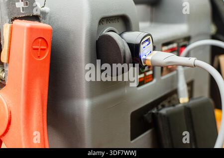 Un primo piano di un dispositivo di avviamento d'emergenza portatile multifunzione e di un power Bank, con cavi di ricarica USB collegati e morsetti per batterie per impieghi pesanti per e. Foto Stock