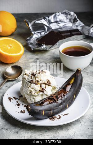 Dolce dolce. Banana grigliata con cioccolato fondente, succo di agrumi e gelato alla vaniglia Foto Stock