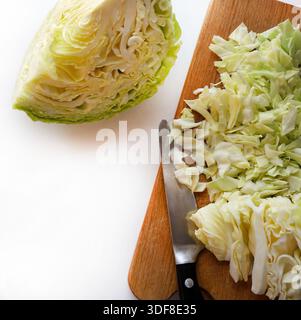​​cabbage tagliato finemente o cavolo Savoy su un tagliere di legno, accanto alla metà di un altro cavolo su sfondo bianco. Cibo sano e vegetariano. Foto Stock