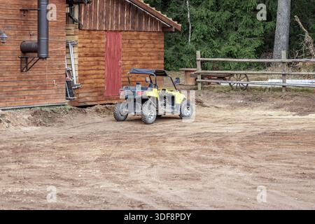 Buggy UTV giallo parcheggiato su un terreno sterrato accanto a una rustica cabina in legno. Concetto di trasporto fuoristrada, lavoro agricolo e avventura all'aria aperta. Foto Stock