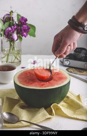 Il cucchiaio con pezzo di anguria in mano uomo Foto Stock