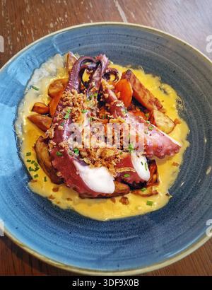 Piatto splendidamente placcato di teneri tentacoli di polpo grigliati servito su patate dolci arrostite dorate e salsa cremosa, guarnito con croccanti fritti Foto Stock