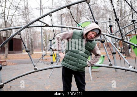 Un uomo con tuta e cappello si piega su un terreno sportivo all'aperto. Esercizio fisico a basse temperature. Foto Stock