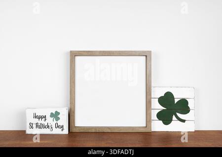 Montatura in legno con decorazioni in stile St Patricks Day su un ripiano in legno. Eleganti insegne in legno. Cornice quadrata contro una parete bianca. Copia spazio. Foto Stock