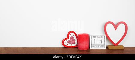 Decorazioni di San Valentino con cuore, candele e calendario in legno rustico. Ripiano in legno contro uno striscione bianco. Copia spazio. Foto Stock
