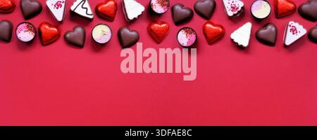 San Valentino, cioccolato al top border. Tema del cuore rosso e rosa. Vista dall'alto su uno sfondo rosso per striscioni con spazio di copia. Foto Stock