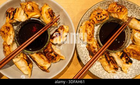Due ciotole di gyoza fritta in padella con bacchette e salsa di soia al centro. Informale, condivisibile, pronto a mangiare. Perfetto per cene sociali e spuntini asiatici Foto Stock
