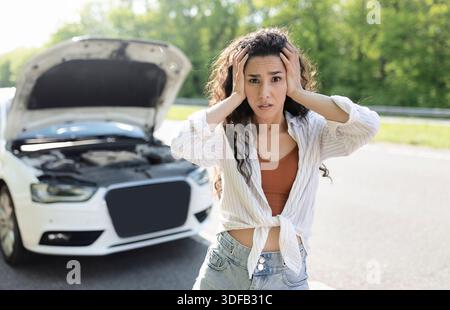Giovane donna stressata in piedi su autostrada vicino a macchina rotta, afferrare la testa nel terrore, in attesa di guasto servizio stradale Foto Stock