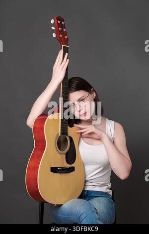 Giovane musicista donna che tiene la classica chitarra acustica a sei corde in verticale accanto a lei, abbraccia lo strumento musicale, spinge la chitarra spagnola verso la sua Foto Stock