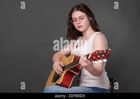 Chitarrista femminile che esegue un pezzo di musica alla chitarra classica. Musicista che indossa gli occhiali concentrandosi sulle corde. Giovane donna europea adulta musi Foto Stock
