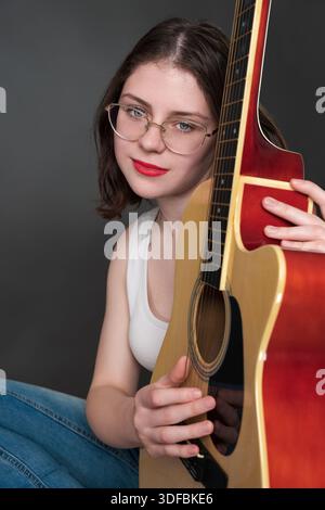 Chitarrista donna con un'espressione emotiva positiva, che tiene la chitarra verticalmente e abbraccia delicatamente lo strumento musicale. diciottenne musicista belo Foto Stock