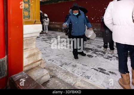 Un operaio distribuisce sale per sciogliere il ghiaccio nella città Proibita ricoperta di neve a Pechino, in Cina. Manutenzione invernale presso lo storico Palace Museum. Foto Stock