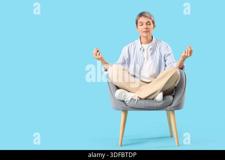 Donna matura che medita in poltrona su sfondo blu Foto Stock