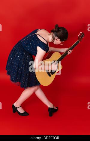 La chitarrista giocosa musicista rock suona la chitarra acustica, si piega in avanti in una raffica di ispirazione musicale, ballando sul palco durante l'esibizione. Fu Foto Stock