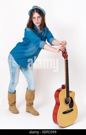 Giovane chitarrista donna in piedi in avanti si piega a tutta lunghezza, appoggiandosi le mani su una chitarra classica verticale di fronte a lei. fe di 18 anni Foto Stock
