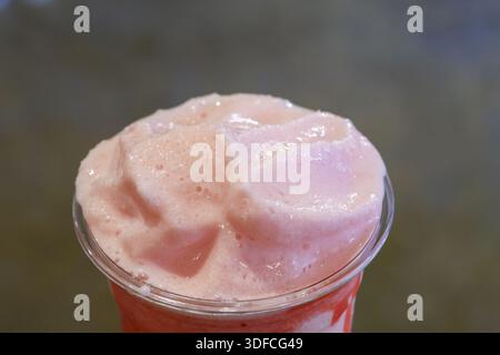 Rinfrescante frullato rosa freddo con consistenza dolce schiumosa servito in una tazza di plastica trasparente che offre un delizioso sapore di fragola ghiacciata, perfetto per il summ caldo Foto Stock