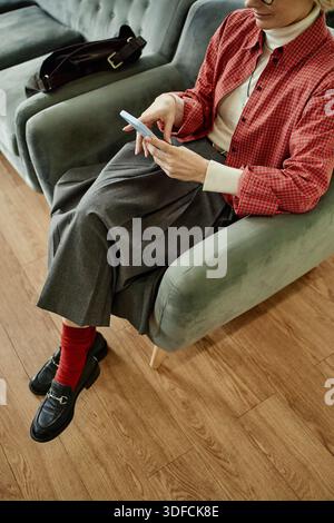 Donna caucasica di mezza età che usa lo smartphone mentre è seduta in poltrona Foto Stock