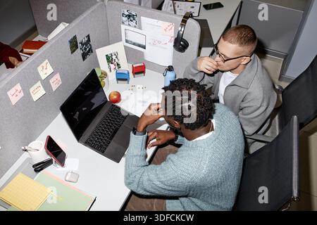 Giovane uomo caucasico e giovane uomo nero che collaborano a Office Workstation Foto Stock