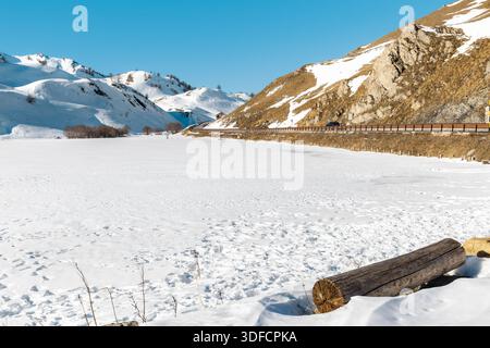 Vista panoramica invernale del lago innevato circondato da pendii innevati sul passo montano del Colle della Maddalena in Piemonte. Foto Stock