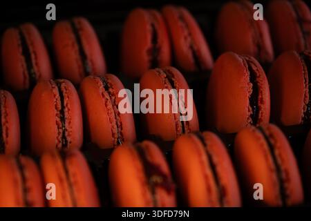 File di vivaci macaron di fragole rosse con gusci delicati e ripieno di frutta, presentati come un classico dessert francese Foto Stock